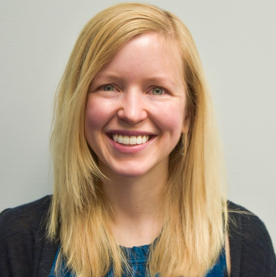 a woman with blond hair stands against a cream colored wall