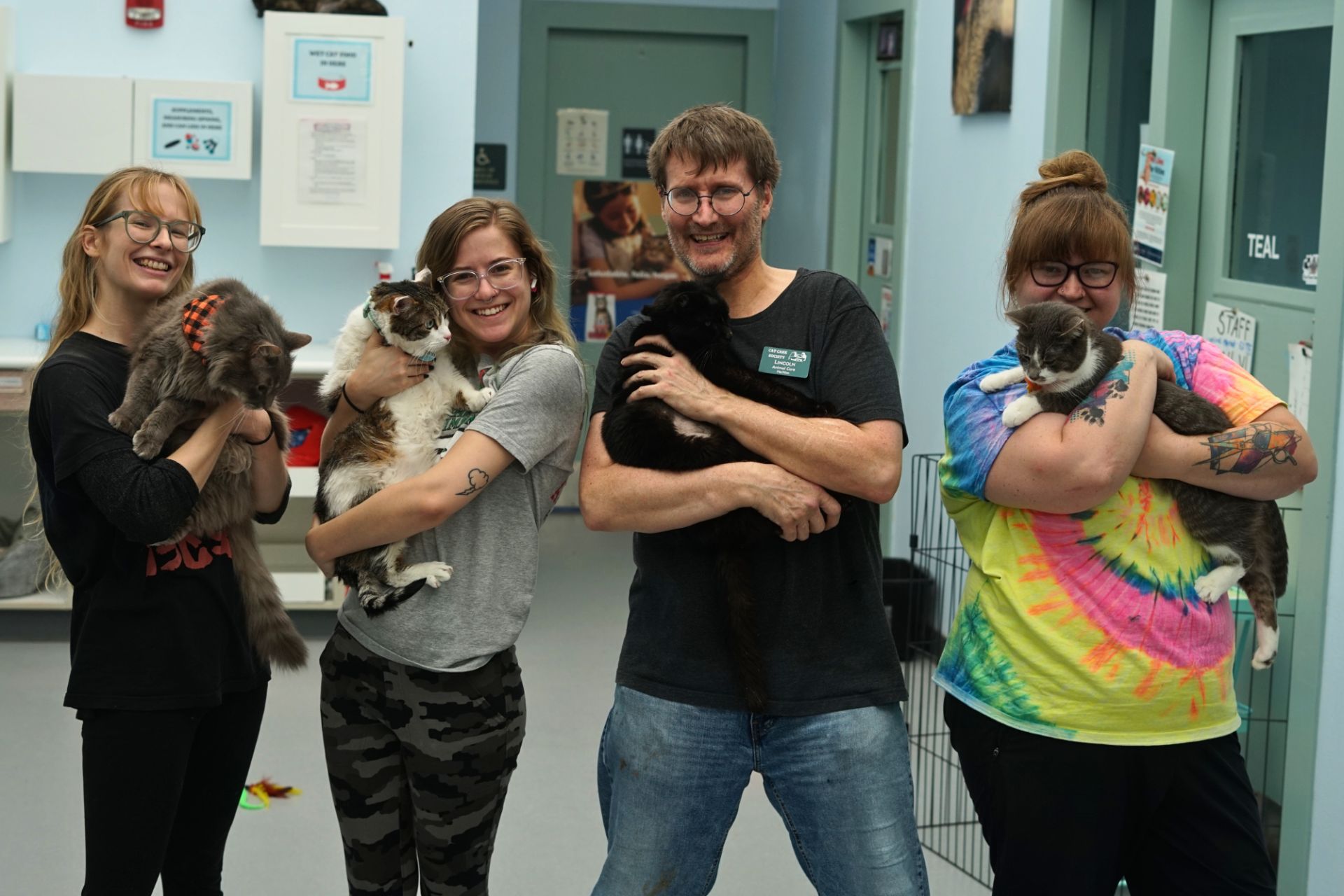 four people hold cats in a shelter